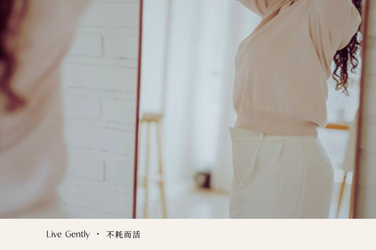 A person pausing in front of a mirror, adjusting their clothing in soft morning light.