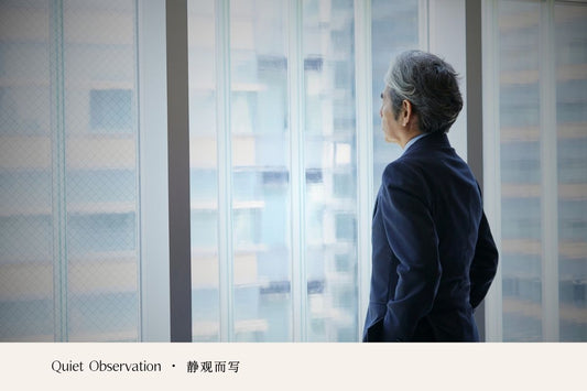 A person standing by a large window, quietly looking out at the city.