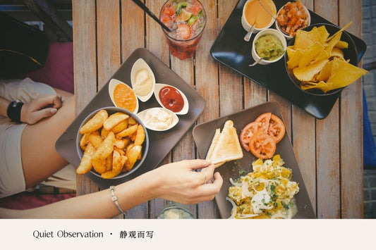 A table with shared meals, drinks, and hands reaching for food during a quiet gathering.